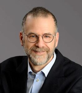 A photo of Corey Glickman is captured. He is the Vice President at Infosys and leads their sustainability and design business. Corey is featured on the Practice of the Practice, a therapist podcast.